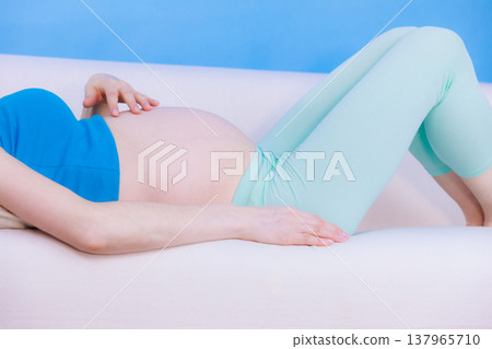 Pregnant woman lying on couch touching her belly Pregnant woman lying on couch touching her belly 137965710