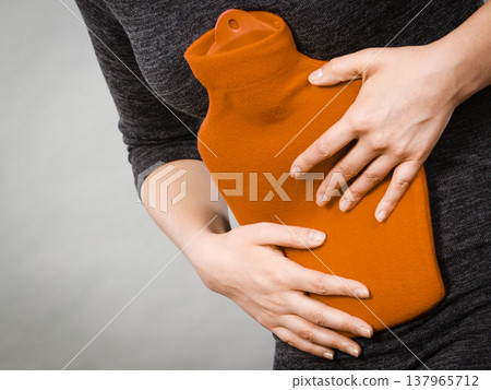 Girl having stomach ache, holding hot water bottle 137965712
