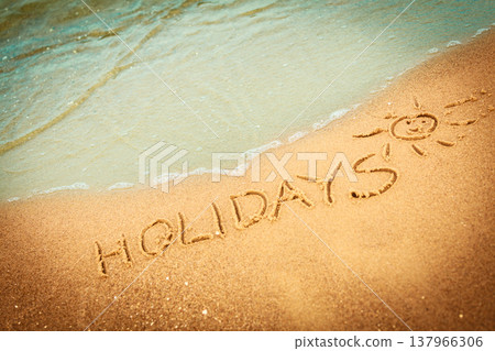 The word holidays written in the sand on a beach The word holidays written in the sand on a beach 137966306