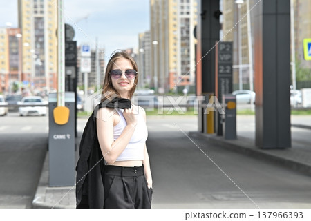 Woman walking in stylish outfit holding sunglasses near modern geometric wall. Woman walking in stylish outfit holding sunglasses near modern geometric wall. 137966393