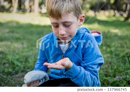 Child exploring nature holding small snail in hand outdoors, curiosity and focus, learning through play Child exploring nature holding small snail in hand outdoors, curiosity and focus, learning through play 137966745