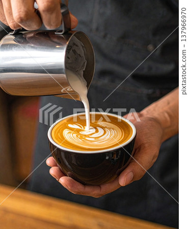A skilled barista carefully pours steamed milk into a dark ceramic cup A skilled barista carefully pours steamed milk into a dark ceramic cup 137966970