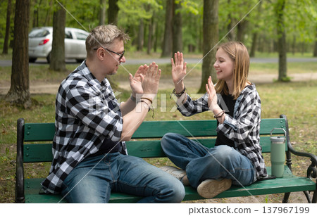 Happy Father And Little Daughter Sitting On A Bench Play A Clapping Game In Family Look Happy Father And Little Daughter Sitting On A Bench Play A Clapping Game In Family Look 137967199