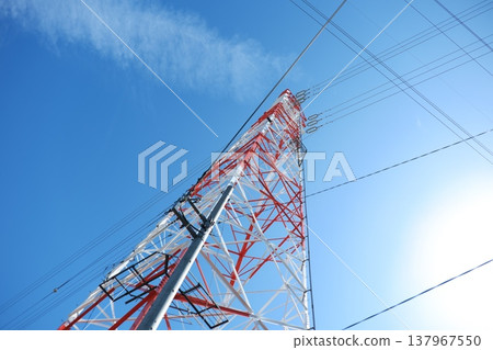 A wide-angle shot of a clear blue sky and red and white transmission towers, bathed in sunlight. 137967550