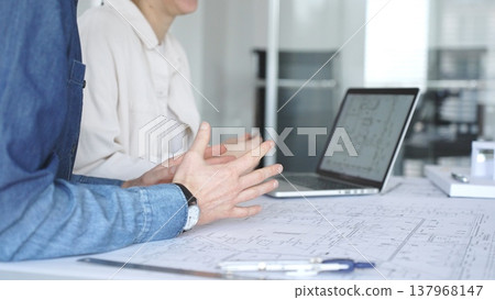 Architects and engineers collaborating on a technical blueprint, discussing construction plans and urban planning details during an office meeting with a laptop displaying cad drawings Architects and engineers collaborating on a technical blueprint, discussing construction plans and urban planning details during an office meeting with a laptop displaying cad drawings 137968147