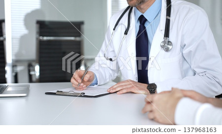 Doctor discussing medical information and treatment plans with a patient during a healthcare consultation in a clinic office. Medicine, healthcare and science concept Doctor discussing medical information and treatment plans with a patient during a healthcare consultation in a clinic office. Medicine, healthcare and science concept 137968163