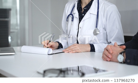 Experienced female doctor consulting patient man, providing medical advice and writing prescription during hospital appointment. Medicine, healthcare and science concept 137968270