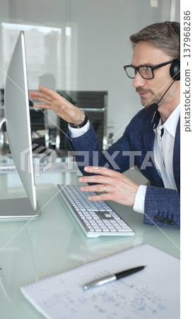 Man in headset talking during online video call, working in office, consulting remote customers, providing technical support. Business people concept Man in headset talking during online video call, working in office, consulting remote customers, providing technical support. Business people concept 137968286