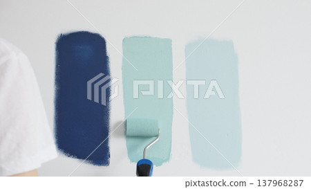 Painter wearing protective gloves rolling blue paint on white wall, creating gradient color effect for home interior renovation project 137968287