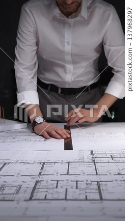 Architect drawing floor plan blueprint with ruler and pen, designing new building construction project. Concept of architecture and business in low key lighting Architect drawing floor plan blueprint with ruler and pen, designing new building construction project. Concept of architecture and business in low key lighting 137968297