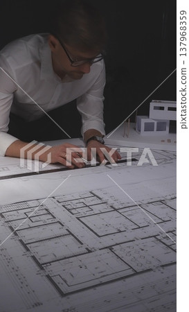 Professional architect working late, drawing blueprints for a new residential construction project. Concept of architecture, planning, and business in low-key lighting 137968359