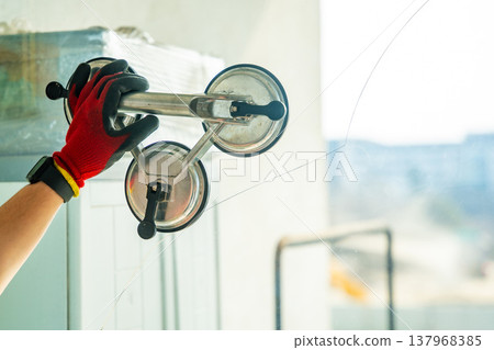 Worker attaching suction cup lifters to cracked window glass before removal from frame during replacement process in apartment. Professional window repair, safe handling, glass installation service Worker attaching suction cup lifters to cracked window glass before removal from frame during replacement process in apartment. Professional window repair, safe handling, glass installation service 137968385