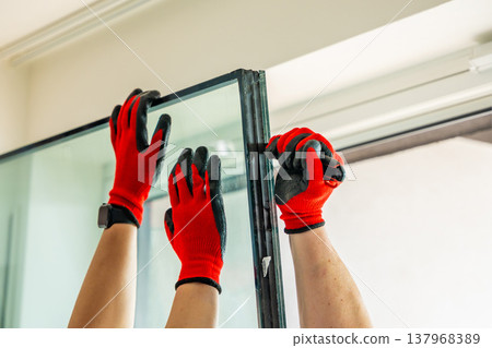 Worker separating triple glazed window glass unit into individual panels for safe handling and disposal after damage in apartment. Window repair, glass recycling and maintenance process concept. Worker separating triple glazed window glass unit into individual panels for safe handling and disposal after damage in apartment. Window repair, glass recycling and maintenance process concept. 137968389