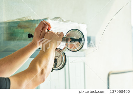 Worker attaching suction cup lifters to cracked window glass before removal from frame during replacement process in apartment. Professional window repair, safe handling, glass installation service 137968400