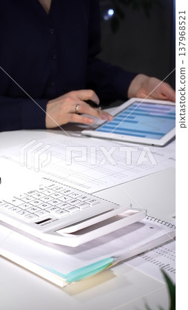 Businesswoman analyzing corporate financial data on a digital tablet in a dimly lit office, managing projects. Audit and taxes in business 137968521