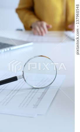 Magnifying glass placed near laptop on white desk, financial papers spread underneath, professional accounting workspace. Audit and taxes in business Magnifying glass placed near laptop on white desk, financial papers spread underneath, professional accounting workspace. Audit and taxes in business 137968548