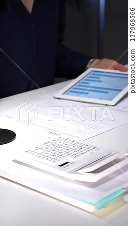 Businesswoman analyzing corporate financial data on a digital tablet in a dimly lit office, managing projects. Audit and taxes in business Businesswoman analyzing corporate financial data on a digital tablet in a dimly lit office, managing projects. Audit and taxes in business 137968566