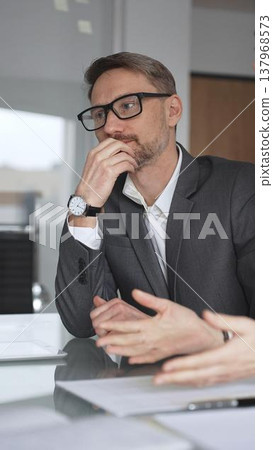 Business colleagues collaborating on an agreement, woman signing a document during a professional meeting in an office, man assisting her with information on a digital tablet, vertical view 137968573