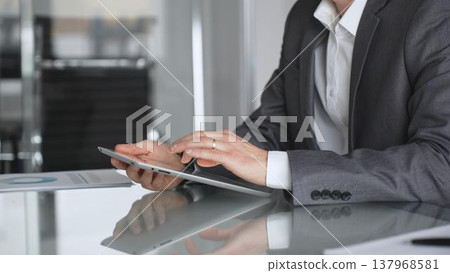 Businessman in a modern office using a digital tablet, managing data and corporate tasks, embracing mobile technology for productivity and efficient communication during a meeting, close up. Businessman in a modern office using a digital tablet, managing data and corporate tasks, embracing mobile technology for productivity and efficient communication during a meeting, close up. 137968581