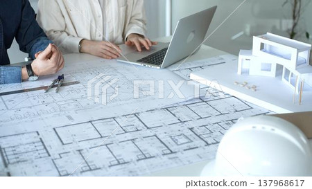 Architects and engineers collaborating on a housing project, designing building blueprints, planning new construction details, and discussing architectural models with a laptop on a desk 137968617