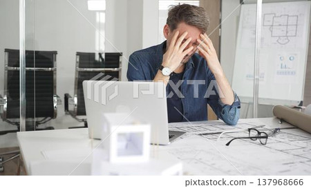 Stressed architect feeling overwhelmed and frustrated, suffering from burnout while working on blueprints for a tight project deadline in a modern office setup 137968666