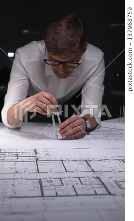 Architect creating technical drawing with compass, designing blueprint on paper for engineering project in office. Concept of architecture and business in low key lighting 137968759