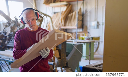Experienced carpenter inspecting wood plank in workshop 137968771