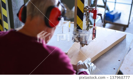 Woodworker cutting wood on band saw with ear protection Woodworker cutting wood on band saw with ear protection 137968777