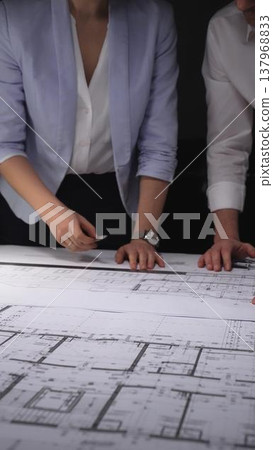 Architects and engineers collaborating on a building blueprint, measuring and discussing plans for a new construction project. Concept of architecture and business in low key lighting Architects and engineers collaborating on a building blueprint, measuring and discussing plans for a new construction project. Concept of architecture and business in low key lighting 137968833