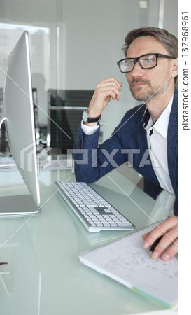 Businessman in a blue jacket thinking and brainstorming ideas while working on computer and taking notes in modern office. Business people concept Businessman in a blue jacket thinking and brainstorming ideas while working on computer and taking notes in modern office. Business people concept 137968961