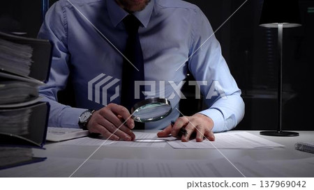 Financial auditor or accountant scrutinizing documents with a magnifying glass and calculator in a dark office. Audit and taxes in business Financial auditor or accountant scrutinizing documents with a magnifying glass and calculator in a dark office. Audit and taxes in business 137969042