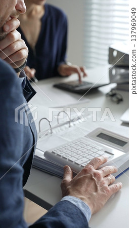 Close up of male accountant hands using calculator while collaborating with female colleague in office, calculating taxes and analyzing financial data. Audit and taxes concept Close up of male accountant hands using calculator while collaborating with female colleague in office, calculating taxes and analyzing financial data. Audit and taxes concept 137969049