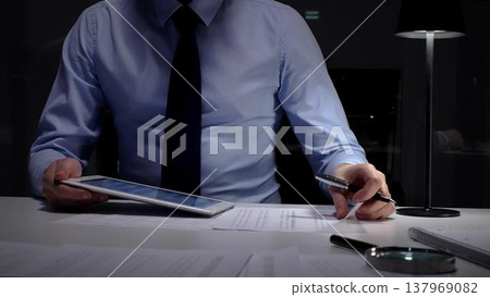 Businessman signing document with a tablet and pen, dedicated to working late in a professional night office. Audit and taxes in business 137969082
