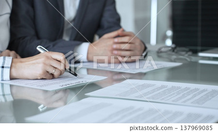 Group of professional business people sitting at a meeting table, reading and discussing contract terms, financial agreements. Collaboration, teamwork, and corporate communication concept Group of professional business people sitting at a meeting table, reading and discussing contract terms, financial agreements. Collaboration, teamwork, and corporate communication concept 137969085