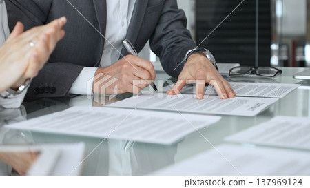 Businessman signing contract documents while female colleague is clapping, finalizing successful partnership agreement. Business people concept 137969124