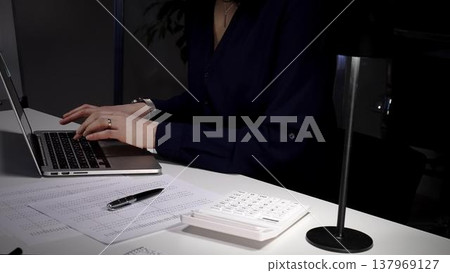 Woman's hands typing on laptop at office desk, working late night with calculator and financial documents. Audit and taxes in business 137969127