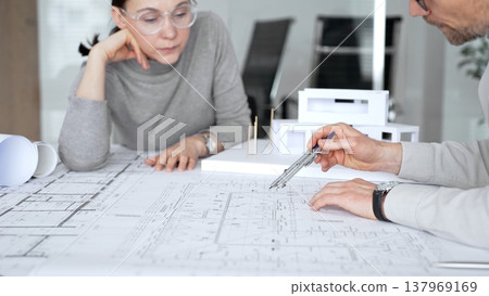 Architectural team analyzing building plans and a white scale model, discussing design concepts and construction details during a professional meeting in an office environment, close up 137969169