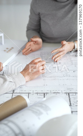 Architects discussing modern building design with 3d model and blueprints during planning meeting focused on innovation, teamwork and sustainable construction solutions, close up Architects discussing modern building design with 3d model and blueprints during planning meeting focused on innovation, teamwork and sustainable construction solutions, close up 137969170