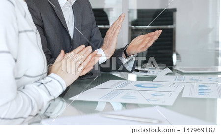 Business colleagues discussing financial reports and charts at meeting table, team applauding successful result. Corporate meeting, business people concept Business colleagues discussing financial reports and charts at meeting table, team applauding successful result. Corporate meeting, business people concept 137969182