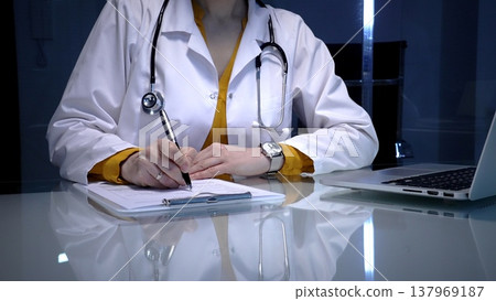 Doctor writing patient medical records, managing data, and documenting information on a clipboard in a clinic setting, utilizing modern technology with a laptop 137969187