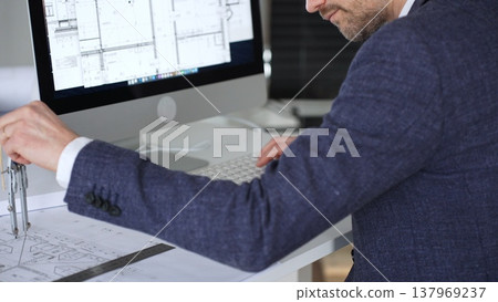 Professional architect drafting blueprints at a desk, holding a compass, focusing on structural plans and urban design. Business and architecture concept 137969237