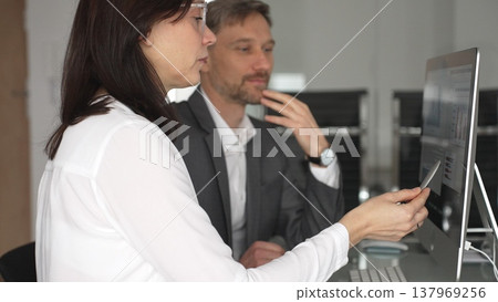 Business colleagues collaborating on data analysis, reviewing financial charts and market trends on a computer screen, discussing strategy and planning outcomes in an office setting. Businesspeople Business colleagues collaborating on data analysis, reviewing financial charts and market trends on a computer screen, discussing strategy and planning outcomes in an office setting. Businesspeople 137969256