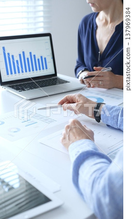 Business professionals working on a laptop, reviewing financial documents, and discussing project strategies in a modern office. Businesspeople and finance concept Business professionals working on a laptop, reviewing financial documents, and discussing project strategies in a modern office. Businesspeople and finance concept 137969384