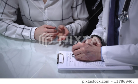 Physician consulting with patient, filling out medical records during a healthcare check up, discussing health concerns and providing treatment information. Overwork in medicine Physician consulting with patient, filling out medical records during a healthcare check up, discussing health concerns and providing treatment information. Overwork in medicine 137969403