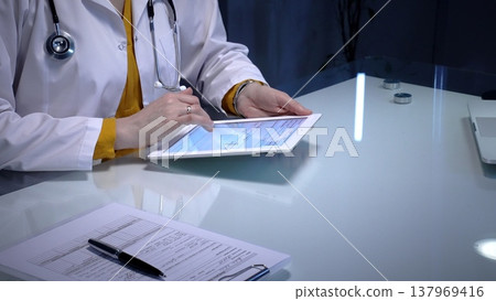 Doctor using digital tablet for remote patient data during an online consultation, managing electronic health records and telehealth services in a modern clinic Doctor using digital tablet for remote patient data during an online consultation, managing electronic health records and telehealth services in a modern clinic 137969416