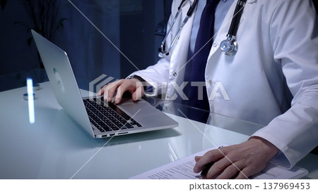 Medical doctor in lab coat with stethoscope typing on laptop in a dim office, managing electronic health records and telemedicine data for modern digital healthcare workflows 137969453