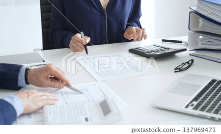 Business team analyzing financial documents, using calculators and laptop, working together on project in modern office. Audit and taxes concept Business team analyzing financial documents, using calculators and laptop, working together on project in modern office. Audit and taxes concept 137969471