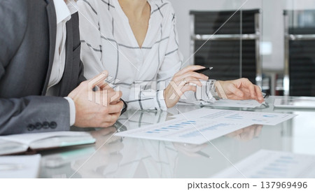 Business people analyzing financial documents during a corporate meeting, discussing data and company strategy Business people analyzing financial documents during a corporate meeting, discussing data and company strategy 137969496