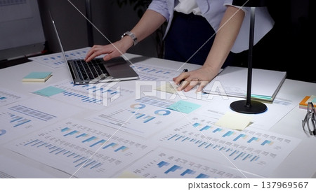 Businesswoman analyzing financial reports and market data on a laptop and paper documents, working late on business strategy and corporate planning in an office Businesswoman analyzing financial reports and market data on a laptop and paper documents, working late on business strategy and corporate planning in an office 137969567