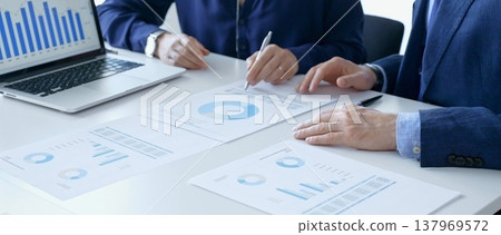 Businessman and business woman reviewing financial documents, gesturing over laptop screen, analyzing market charts for strategic corporate planning. Businesspeople concept 137969572